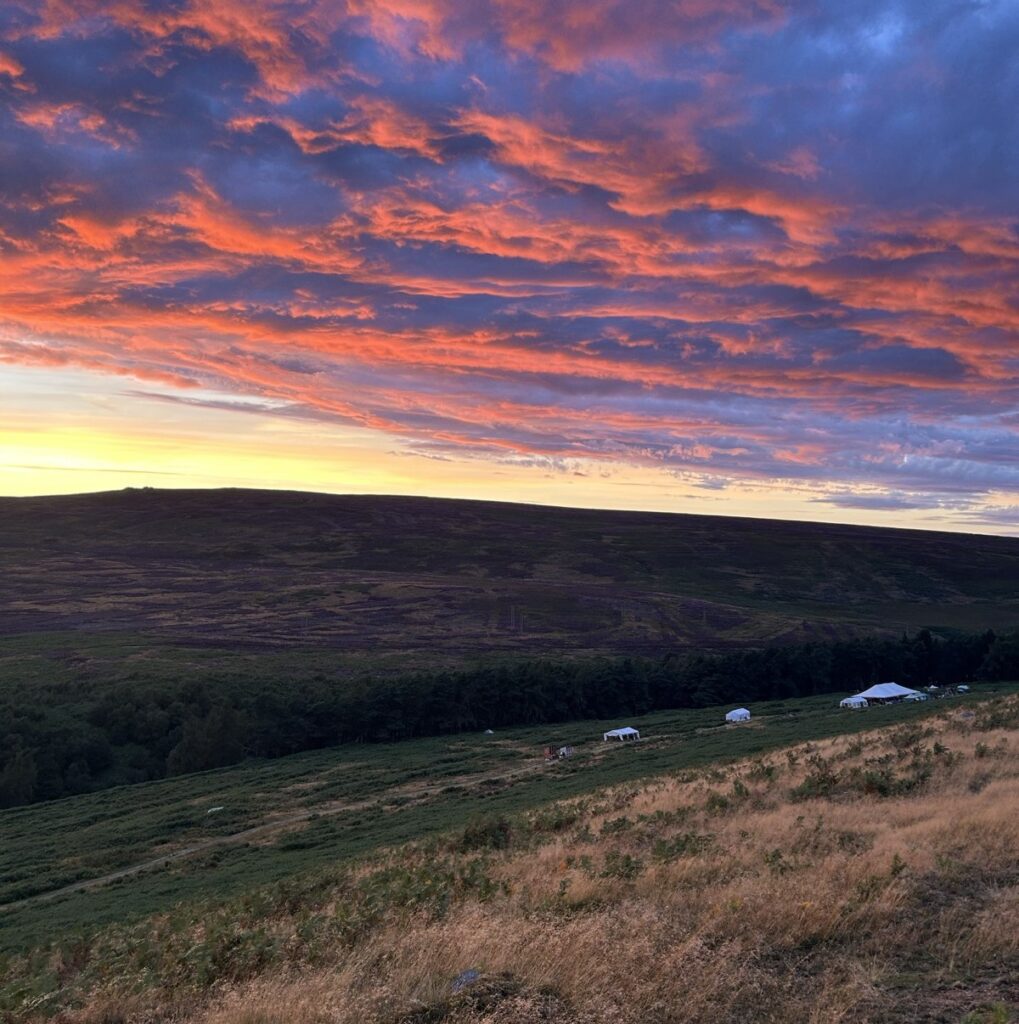 the four main workshop marquees are shown on a heather hillside, with a beautiful red sunset above